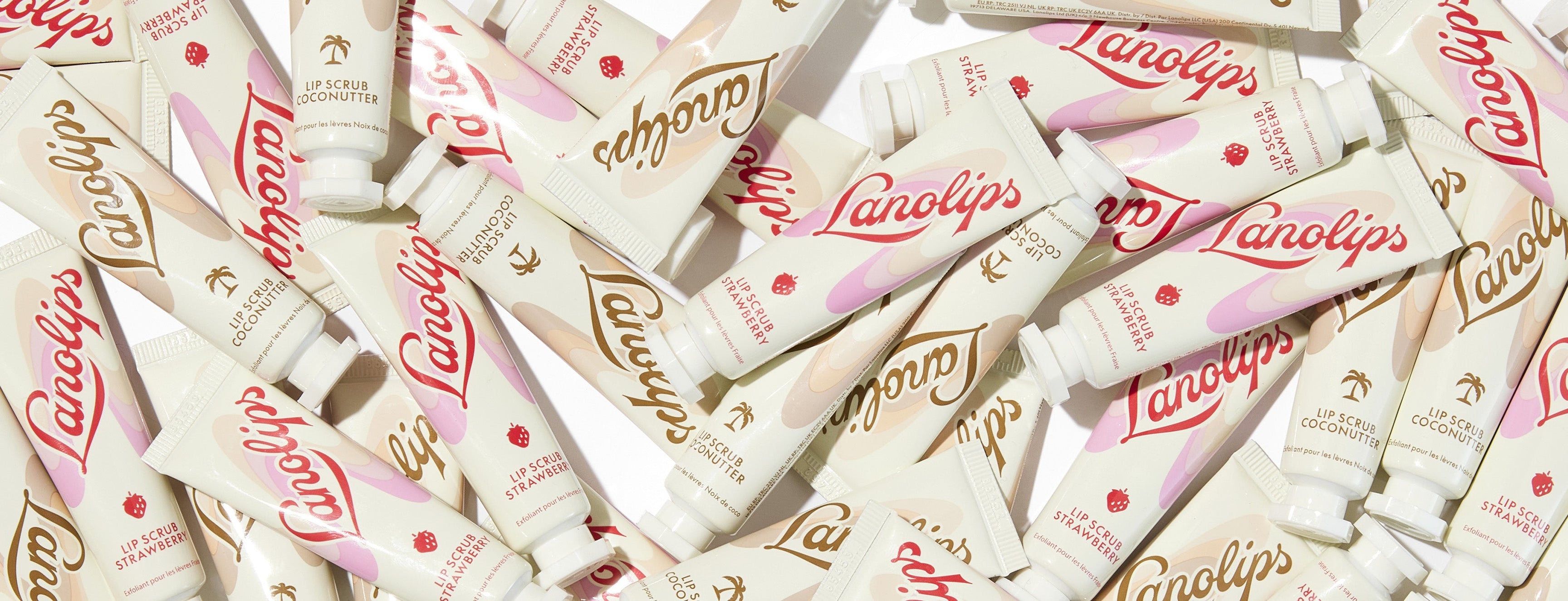 Flat lay of Lanolips Lip Scrubs in Coconutter and Strawberry, scattered around a white background.