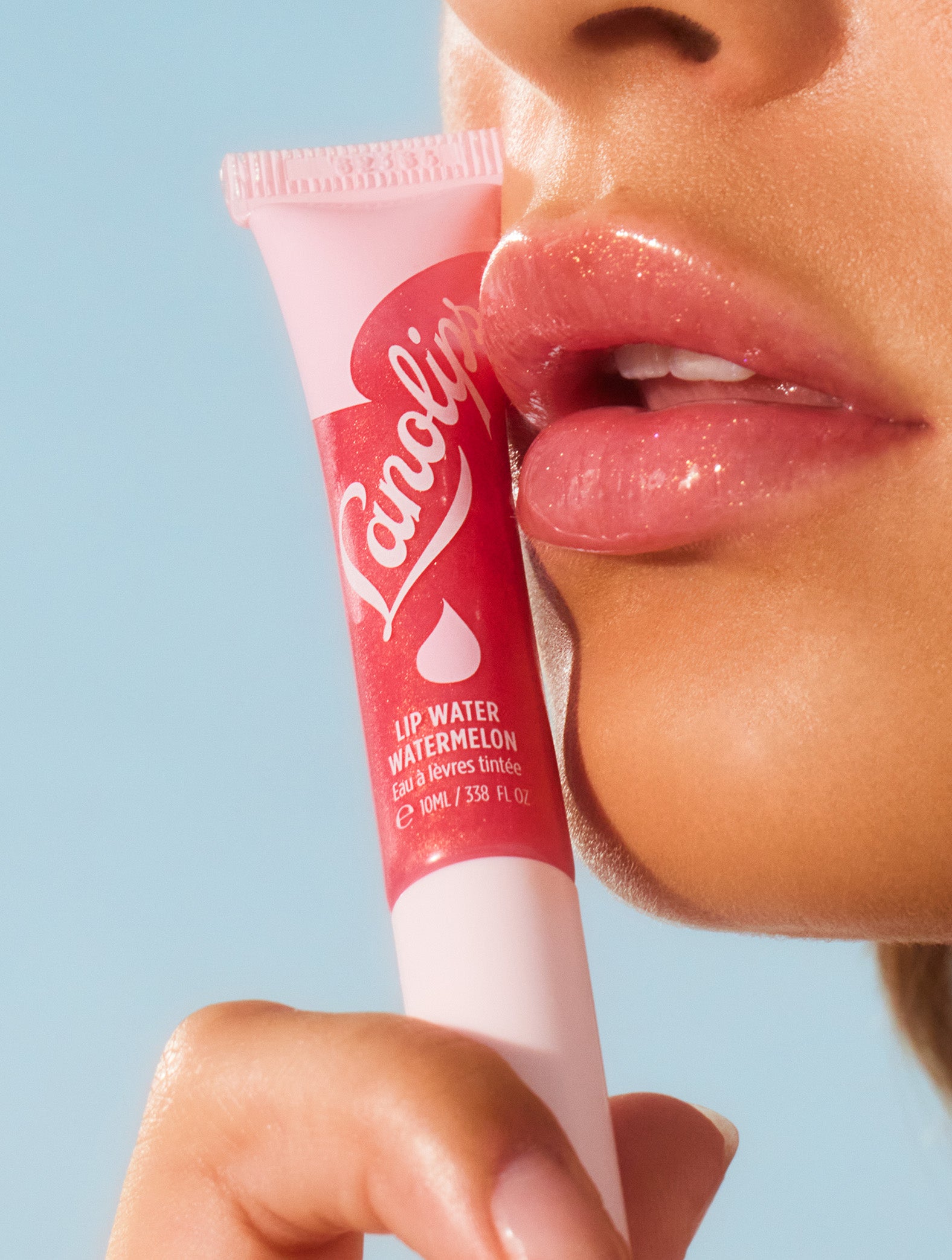 Model wearing Lanolips Lip Water Watermelon on their lips, while holding a tube against her face. Lip Water Watermelon is a sheer wash of pink shimmer that looks radiant on everyone.