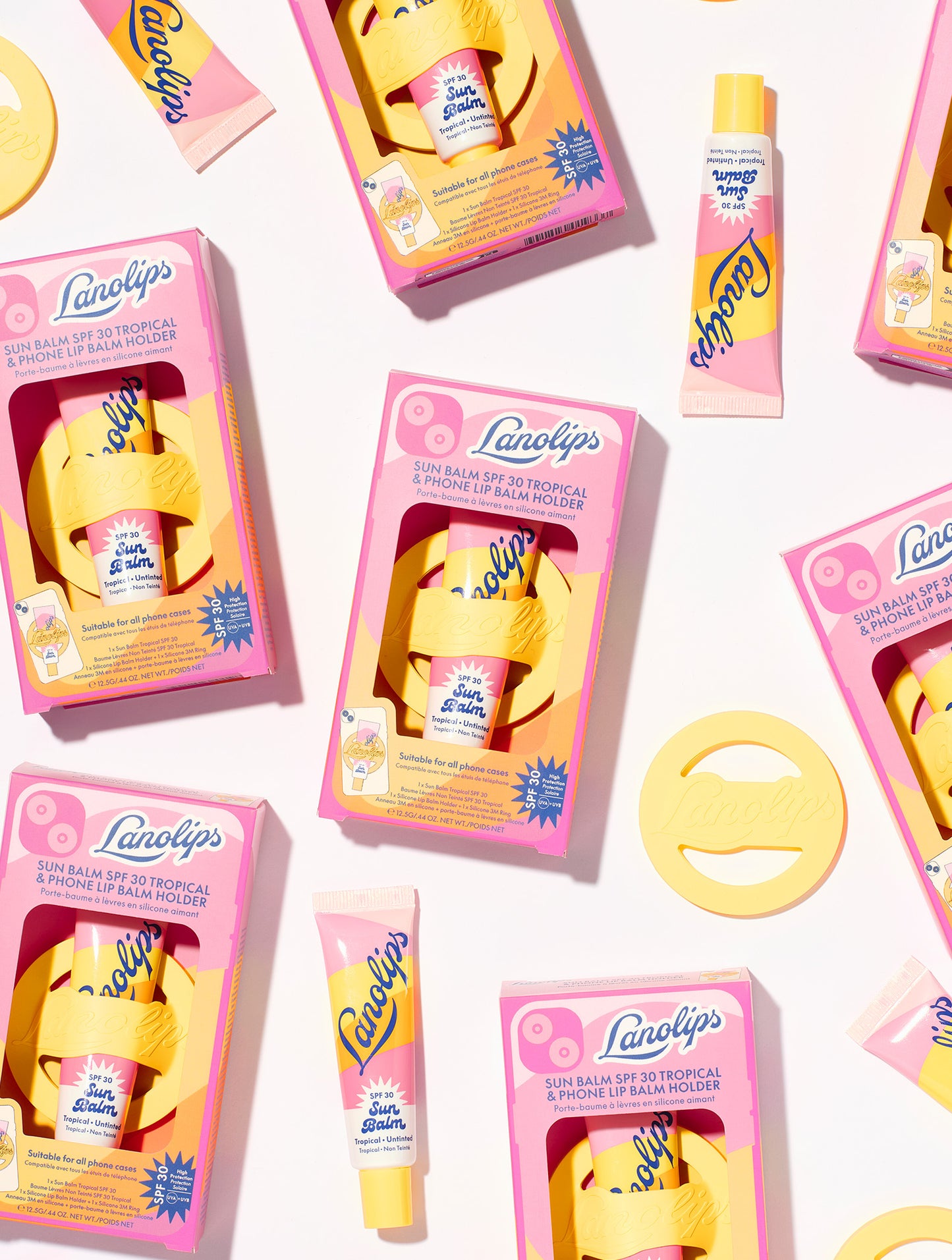 Flat lay of Lanolips Sun Balm SPF 30 Tropical packaging with yellow phone holders and tubes of balm scattered on a white background