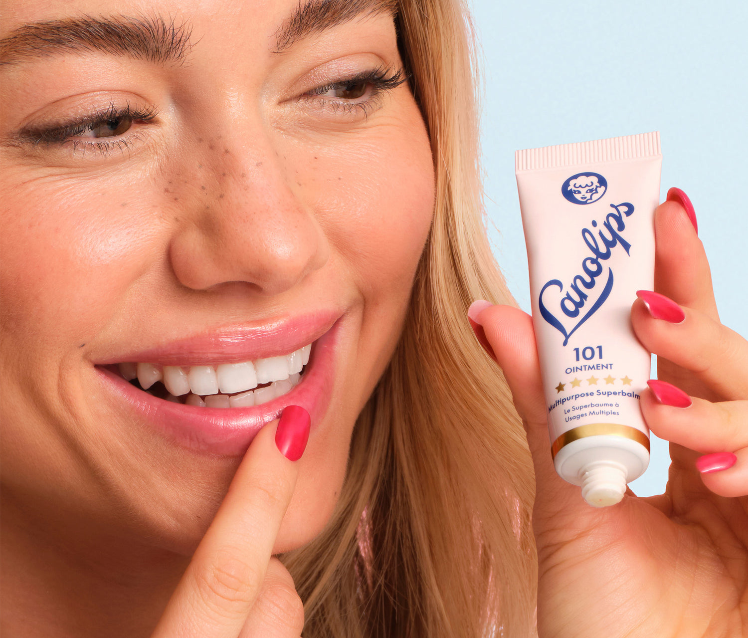 Model applying Lanolips Original 101 Ointment to her lips with a blue background.