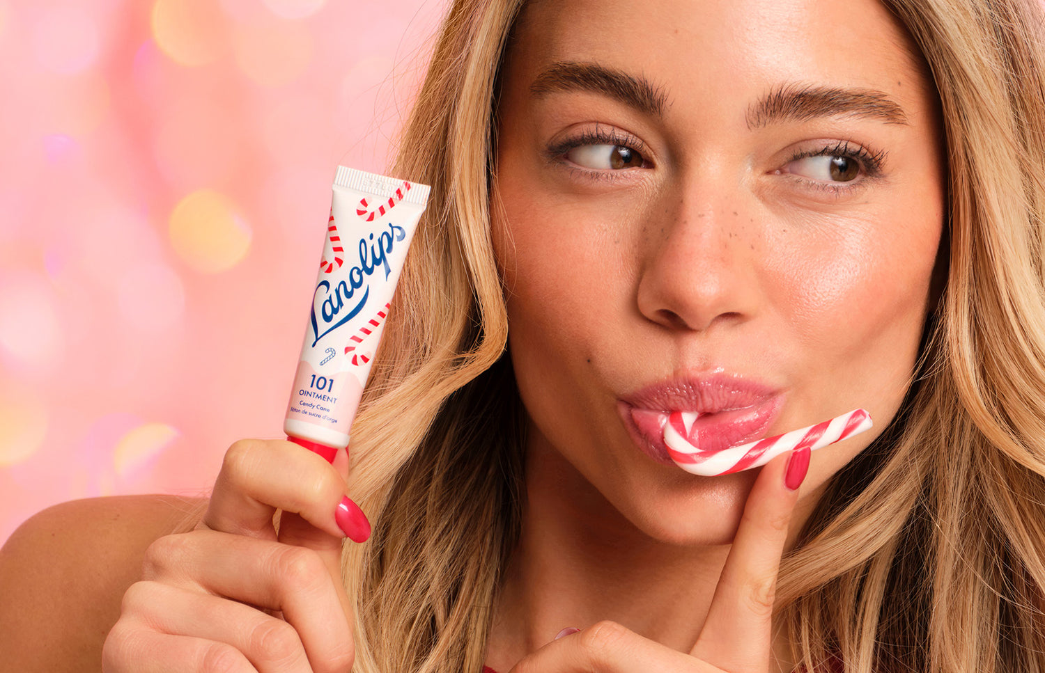 Model holding a tube of Lanolips 101 Ointment Multi Balm Candy Cane against their face, as well as eating a candy cane. The 101 Candy Cane is made with all-natural lanolin, vitamin-e and sweeten peppermint flavor.