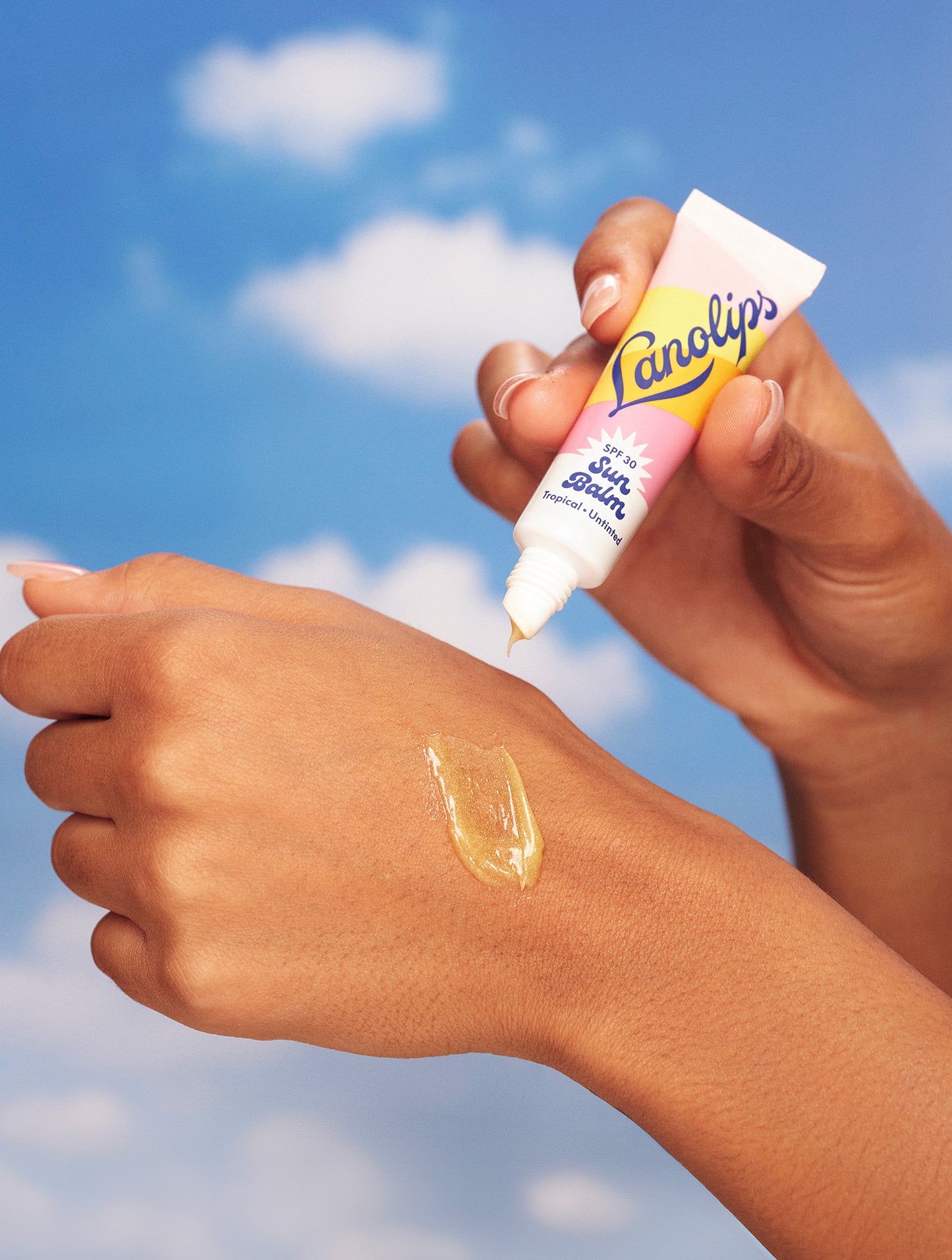 Hands apply Lanolips Sun Balm SPF 30 Tropical on skin, showing its glossy, golden texture - hydrating, protective and tropically nourishing.