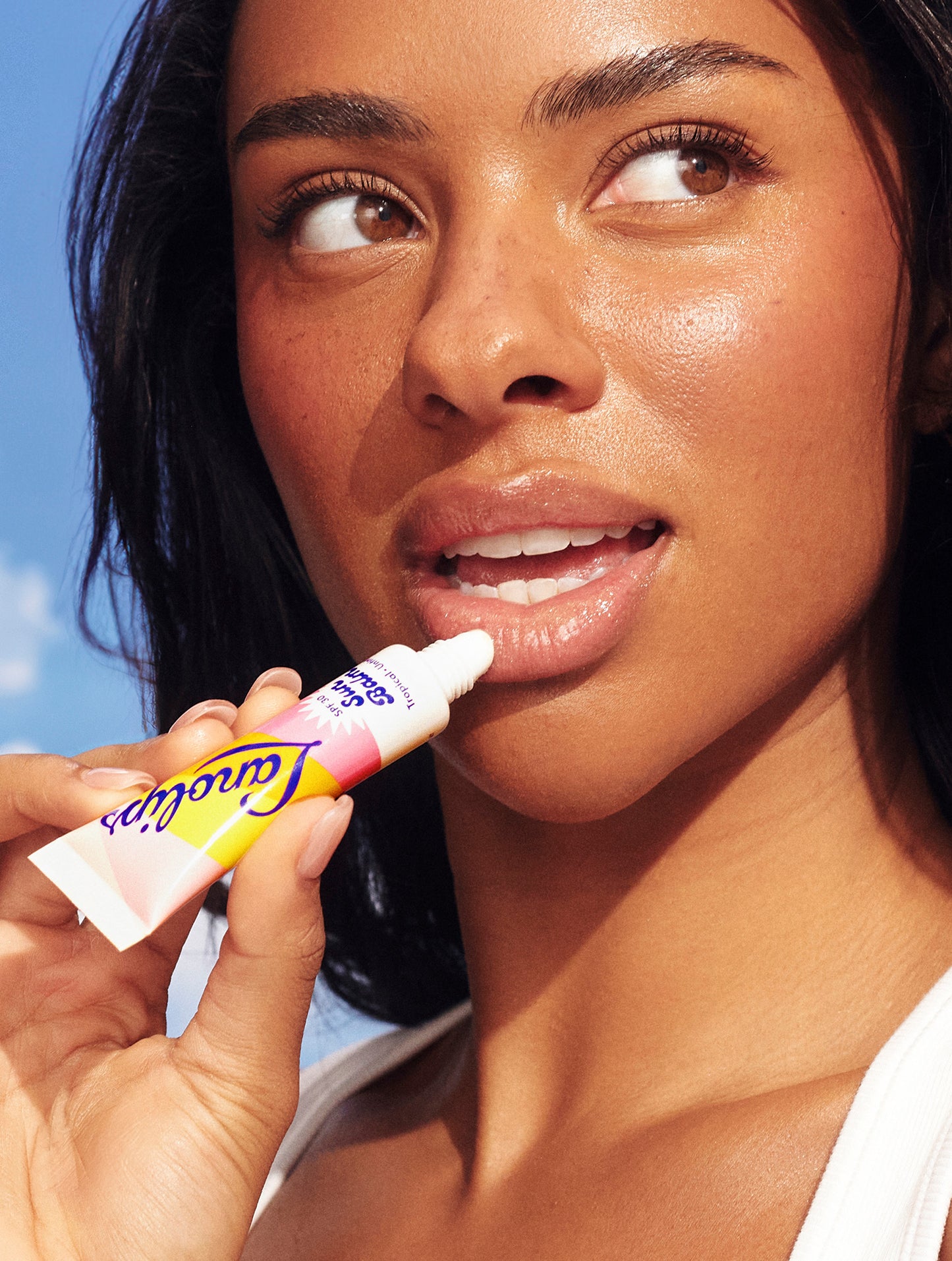 Model applies Lanolips Sun Balm SPF 30 Tropical lip balm. Her glossy, hydrated lips glow in the sun - SPF protection with a nourishing tropical finish.