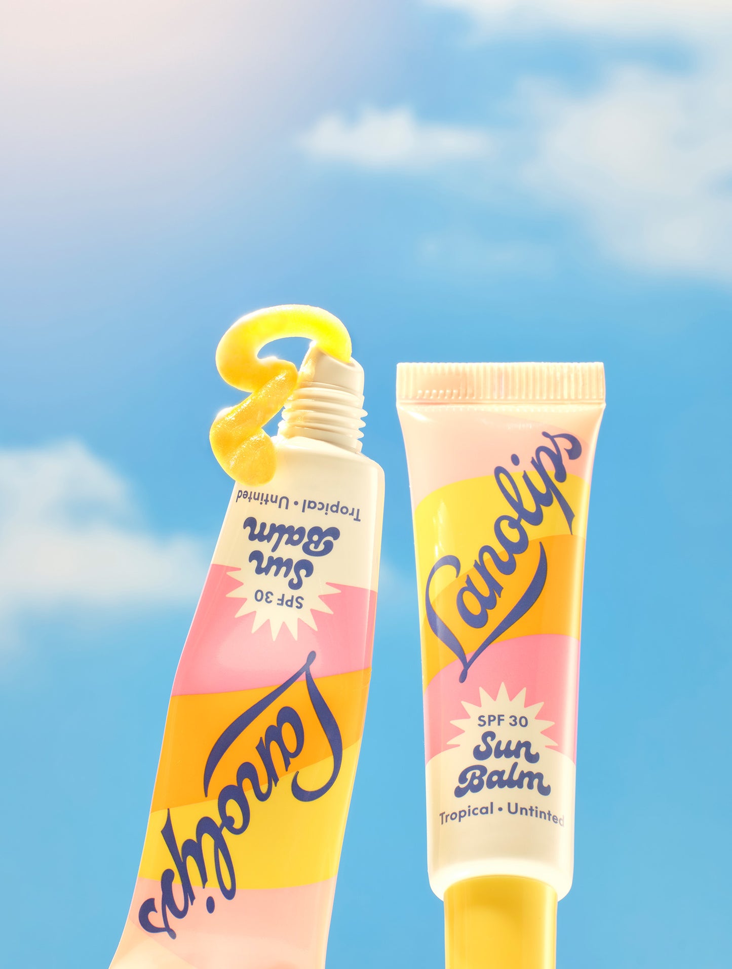 Set against a radiant blue sky with a shining sun, two tubes of Lanolips Sun Balm SPF 30 Tropical lip balm are featured - one standing upright and the other squeezed to reveal a vibrant, glossy balm shaped like a “3” to highlight its SPF 30 protection. This creamy, radiant formula is packed with hydrating lanolin, SPF30 protection. This creamy, radiant formula is packed with hydrating lanolin, SPF
protection, and a luminous sheen.