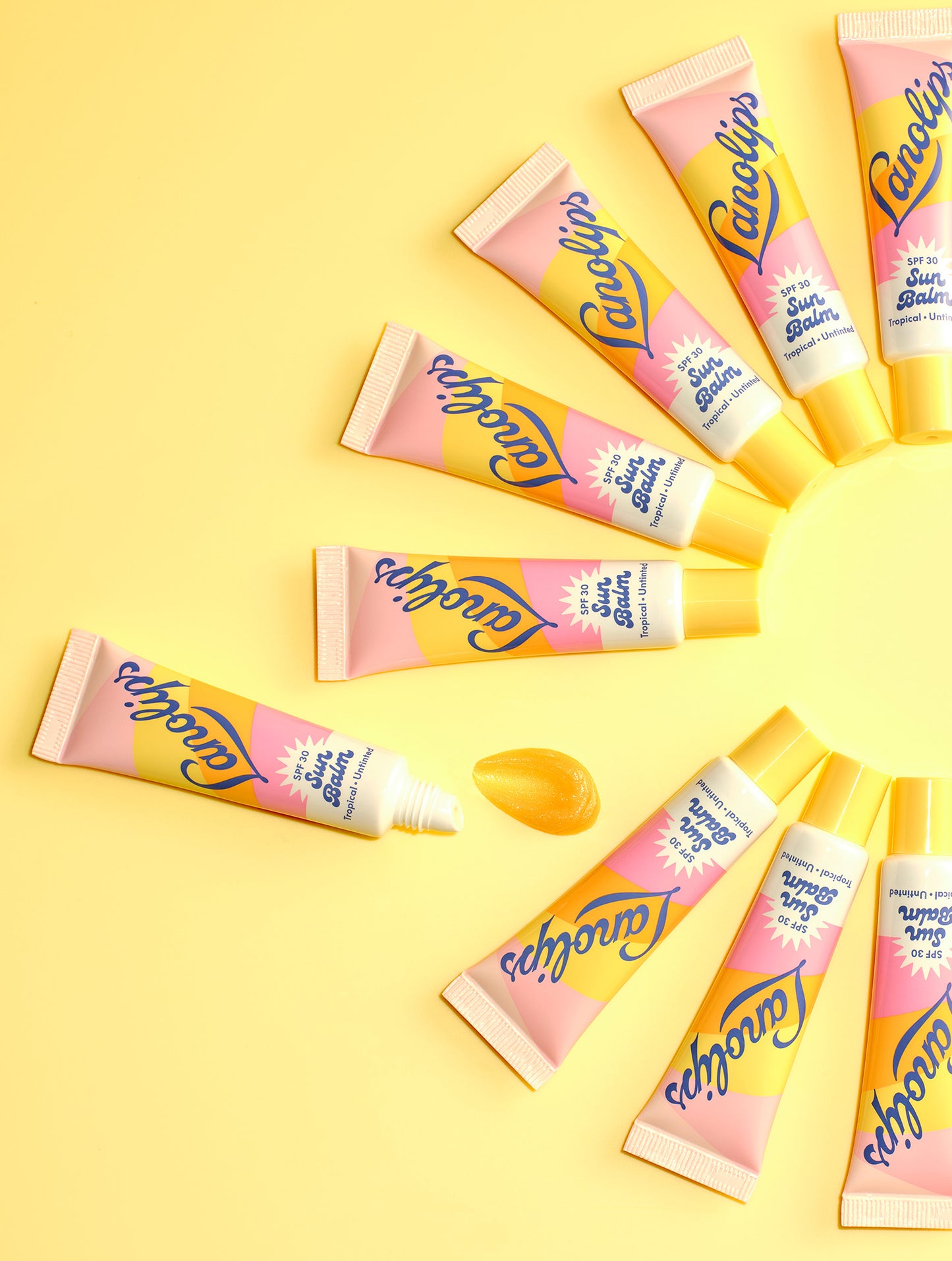 Tubes of Lanolips Sun Balm SPF 30 Tropical arranged in a sun shape on yellow. Hydrating, glossy, untinted SPF balm - your lips’ daily sun visor.