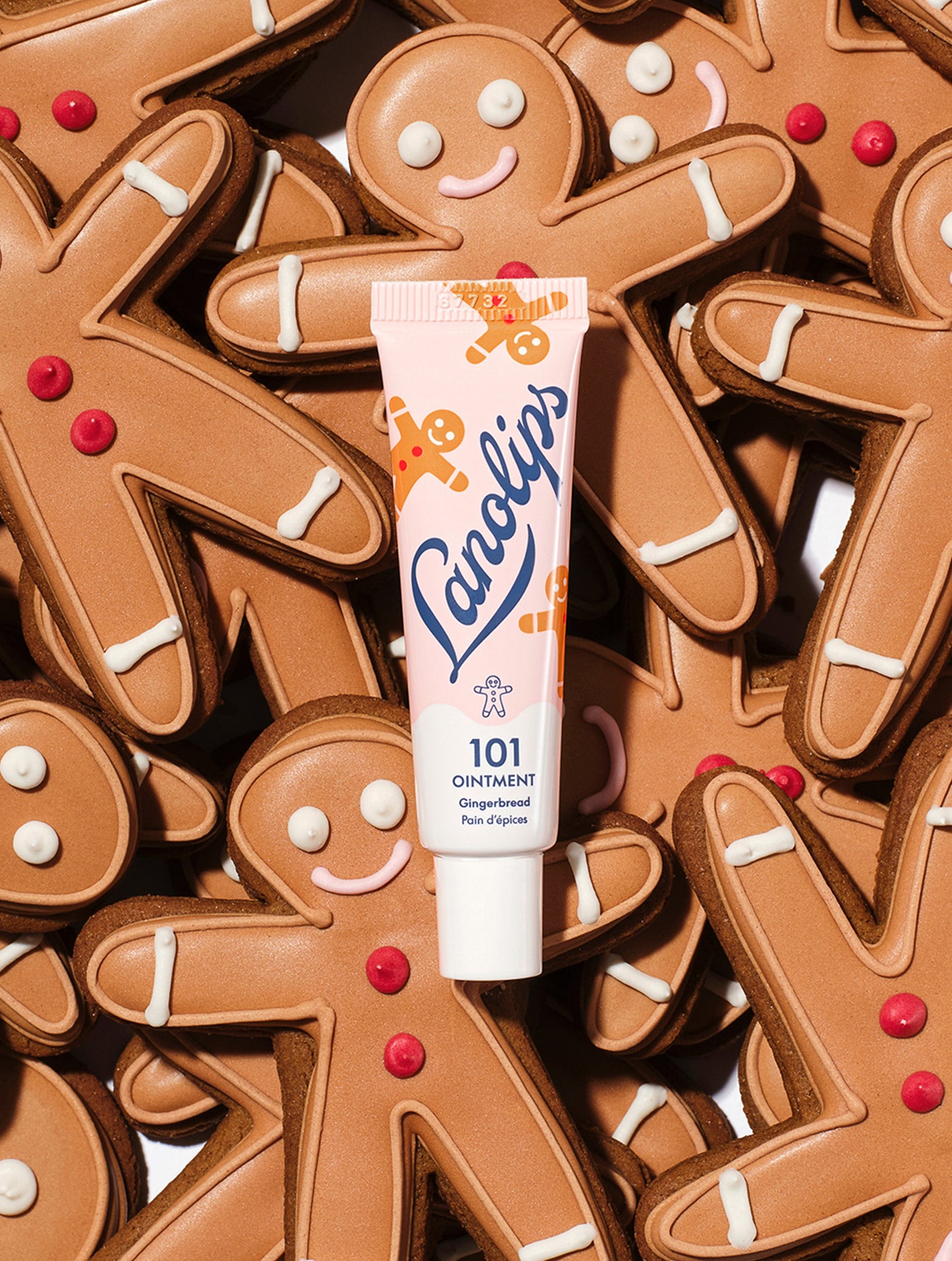 A tube of Lanolips 101 Ointment Multi-Balm Gingerbread surrounded by gingerbread cookies. Embrace warm spice and soft lips with this limited edition festive gourmand flavor.