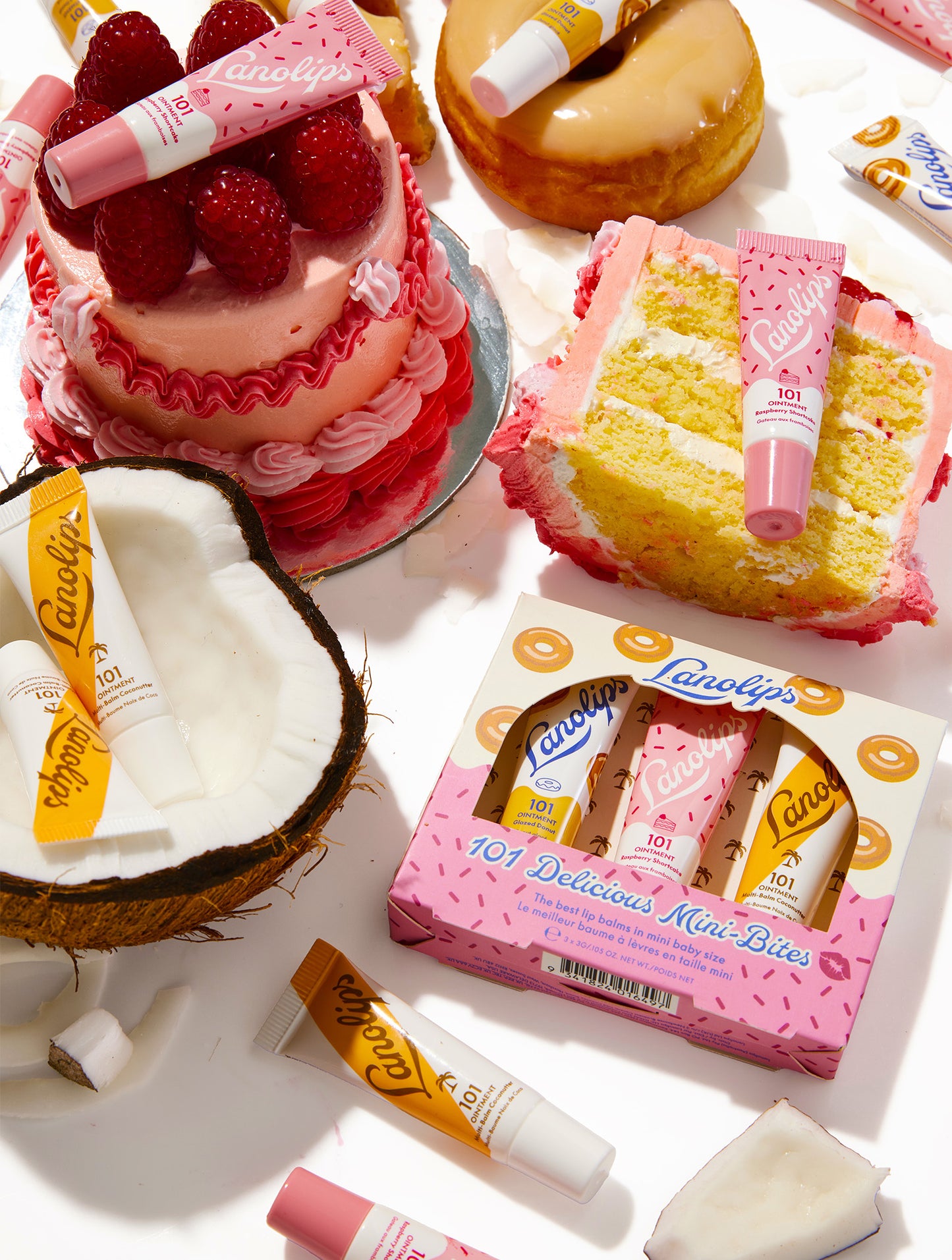 Lanolips 101 Delicious Mini Bites trio set with multiple lip balm tubes surrounded by cake and coconut pieces on a white background.