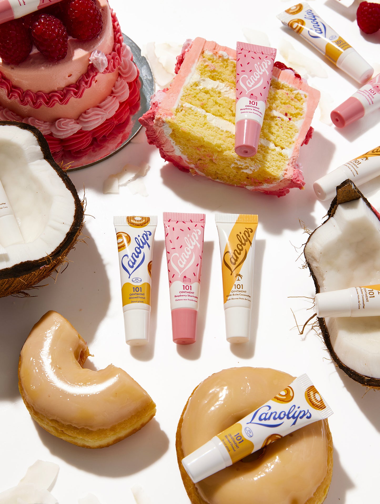Cakes, donuts, and the Lanolips 101 Ointment mini lip balms in Glazed Donut, Raspberry Shortcake and Coconutter on a white background.