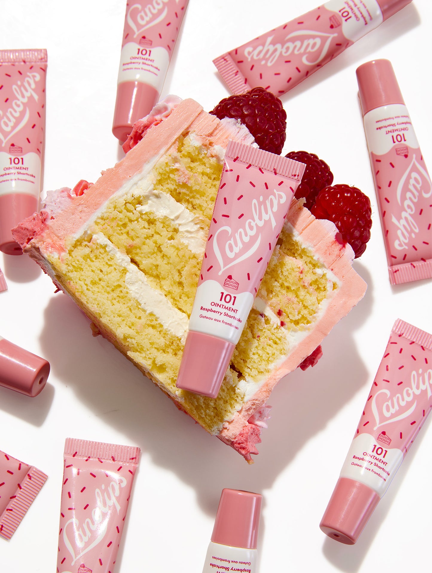 Lanolips 101 Ointment Multi-Balm Raspberry Shortcake mini lip balm tubes with a slice of cake and raspberries on a white background.