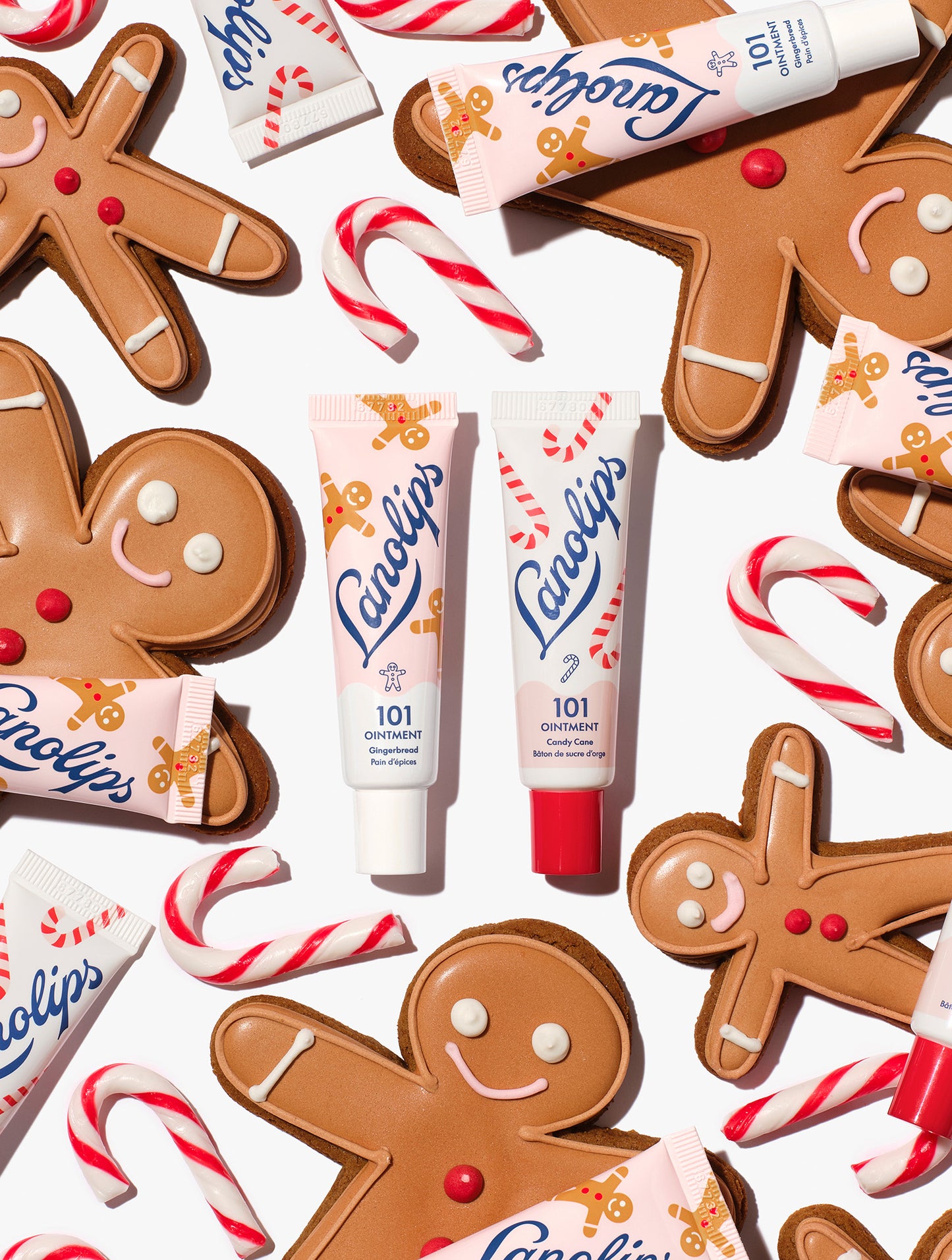 Lanolips 101 Ointment Multi-Balm Gingerbread & Candy Cane centred among gingerbread cookies, candy canes and balm tubes, from the Lanolips Holiday Gingerbread House Lip Duo. Hydrating lanolin, vitamin E and natural flavors keep lips soft and festive.
