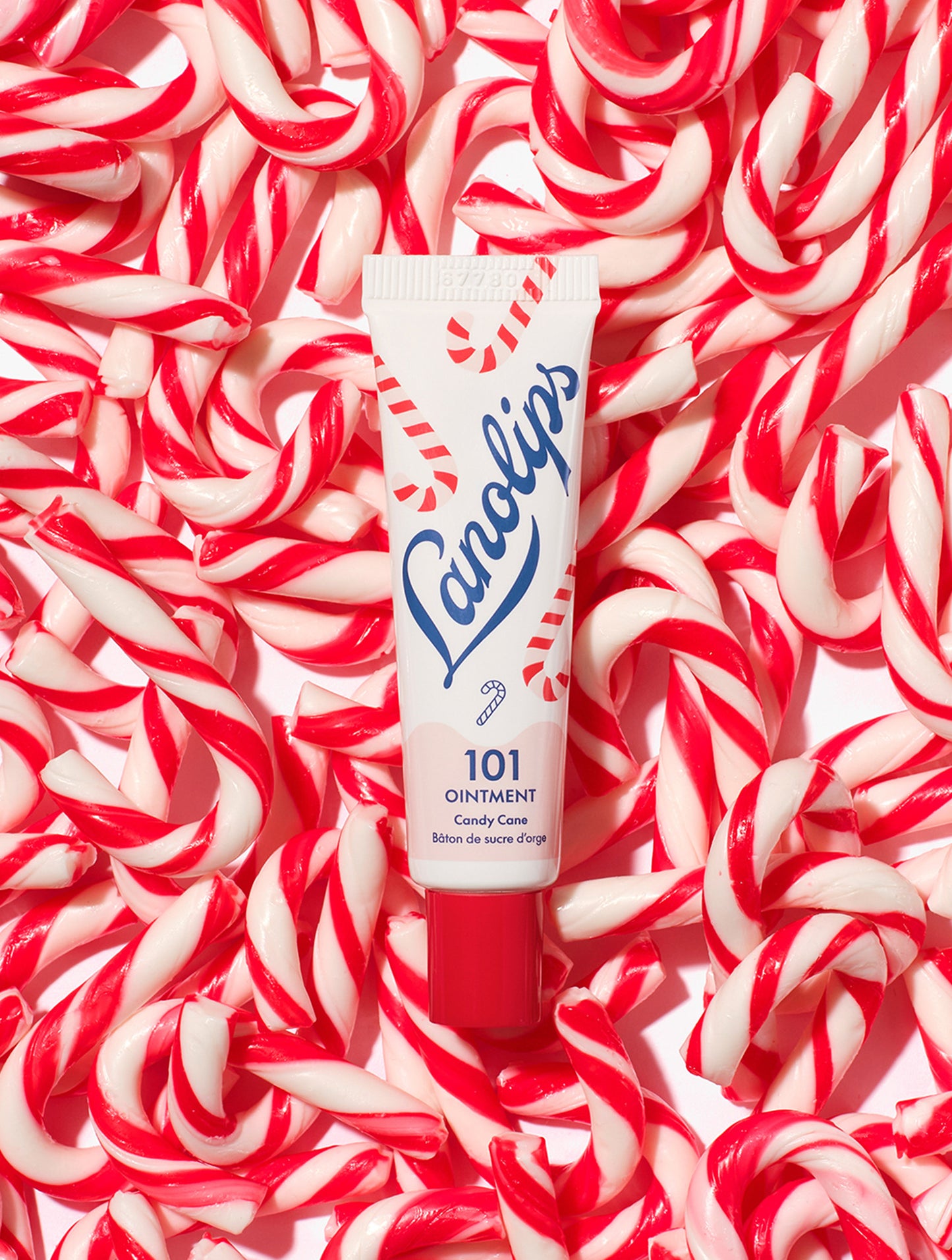 Lanolips 101 Ointment Multi-Balm Candy Cane tube on a background of red and white candy canes. Made with all-natural lanolin, vitamin-e and sweeten peppermint flavor.
