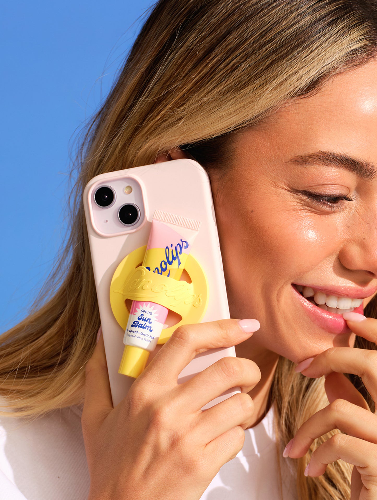 Model holding phone with a tube of Lanolips Sun Balm SPF 30 Tropical Lip Balm and yellow phone lip balm holder attached.