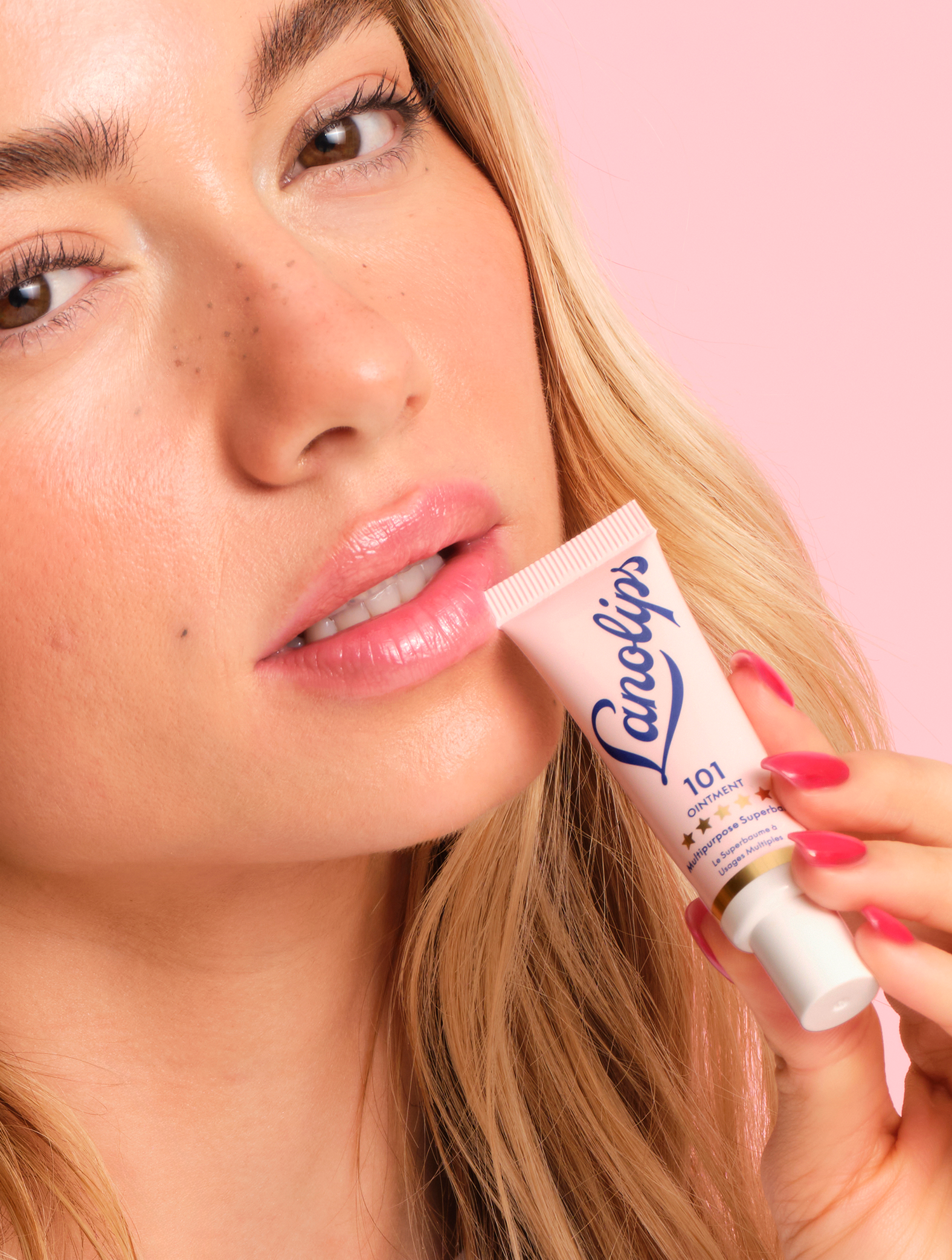 Close up shot of a model holding a Lanolips Original 101 Ointment Multipurpose Superbalm, against a pink background. The World's Best Lip Balm, dermatologically tested, ultra-pure lanolin for lips, skin, cuticles and dry patches.