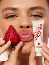 Squeezed tube shot of the Lanolips Lip Scrub Strawberry. A 100% natural balm based scrub that smooth and hydrates. | Load image into Gallery viewer, Model holding Lanolips Lip Scrub Strawberry and with the mixture of ultra-pure grade lanolin, finely ground strawberry seeds and sugar, it leaves your lips deeply hydrated.
