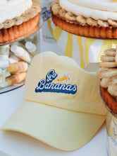 Lanolips Go Bananas Yellow Cap front view. Made with 100% cotton, and the Go Bananas embroidered slogan at the front.  | Load image into Gallery viewer, Lifestyle shot of the 101 Delicious Go Bananas baseball style cap.
