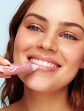 Tinted Lanolin Lip Balm Perfect Nude | Load image into Gallery viewer, A smiling young woman with dewy skin and wavy light brown hair applies Lanolips Tinted Lip Balm in Perfect Nude to her full lips. The hydrating lip balm gives a glossy, natural pink tint, enhancing her radiant complexion.The close-up shot captures the balm’s nourishing texture and smooth application, making it the perfect beauty essential for soft, hydrated lips.
