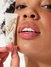 Squeezed tube shot of the Lanolips Lip Scrub Coconutter. A 100% natural balm based scrub that smooth and hydrates. | Load image into Gallery viewer, Model holding Lanolips Lip Scrub Coconutter and with the mixture of ultra-pure grade lanolin, finely grated coconut shell pieces and sugar, it leaves your lips deeply hydrated.
