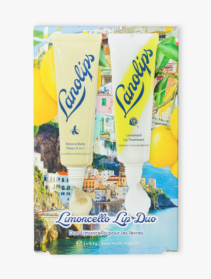 Lanolips Limoncello Lip Duo set features a tube of banana balm lip sheen and a tube of lemonaid lip treatment against a scenic Mediterranean coastal collage background with lemons.