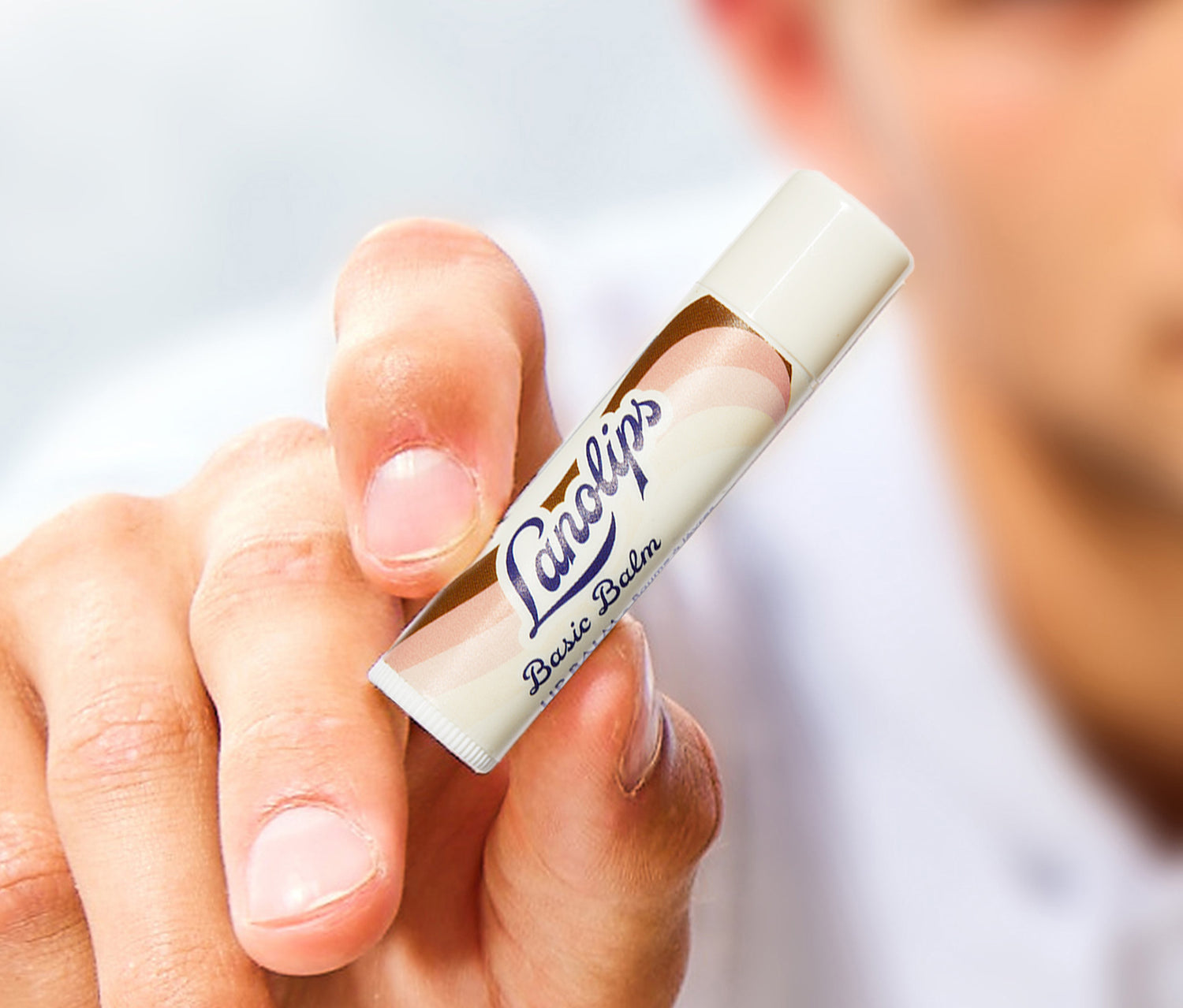 Hand holding a Lanolips Basic Balm Coconutter lip balm stick with a blurred background