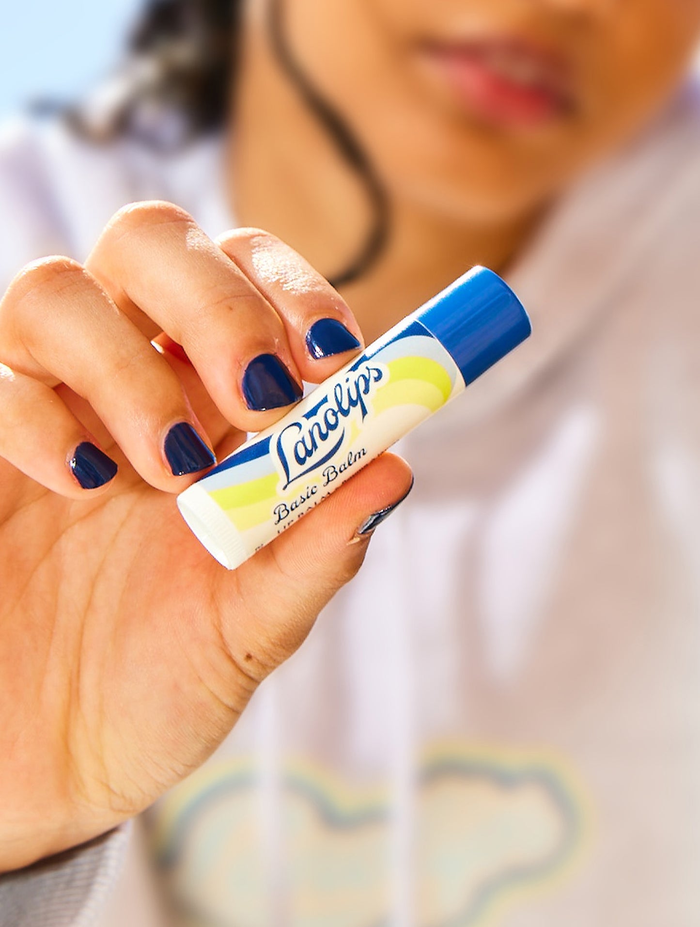 Hand holding a tube of Lanolips Basic Balm Original Vanilla against a blurred background