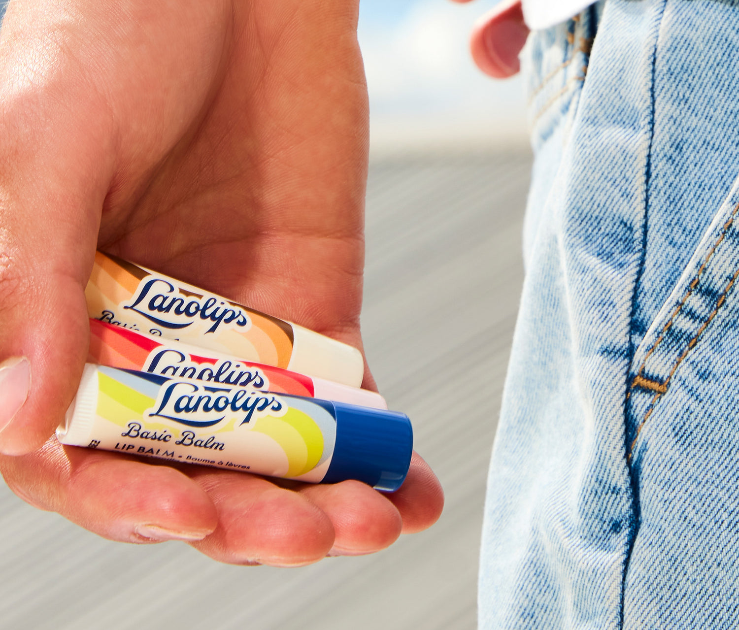 Hand holding three Lanolips Basic Balm tubes. Our Basic Balm range comes in three natural flavours: Coconutter, Strawberry and Original Vanilla. Made with hydrating lanolin, shea butter, vitamin e and combined with natural fruity extracts. 