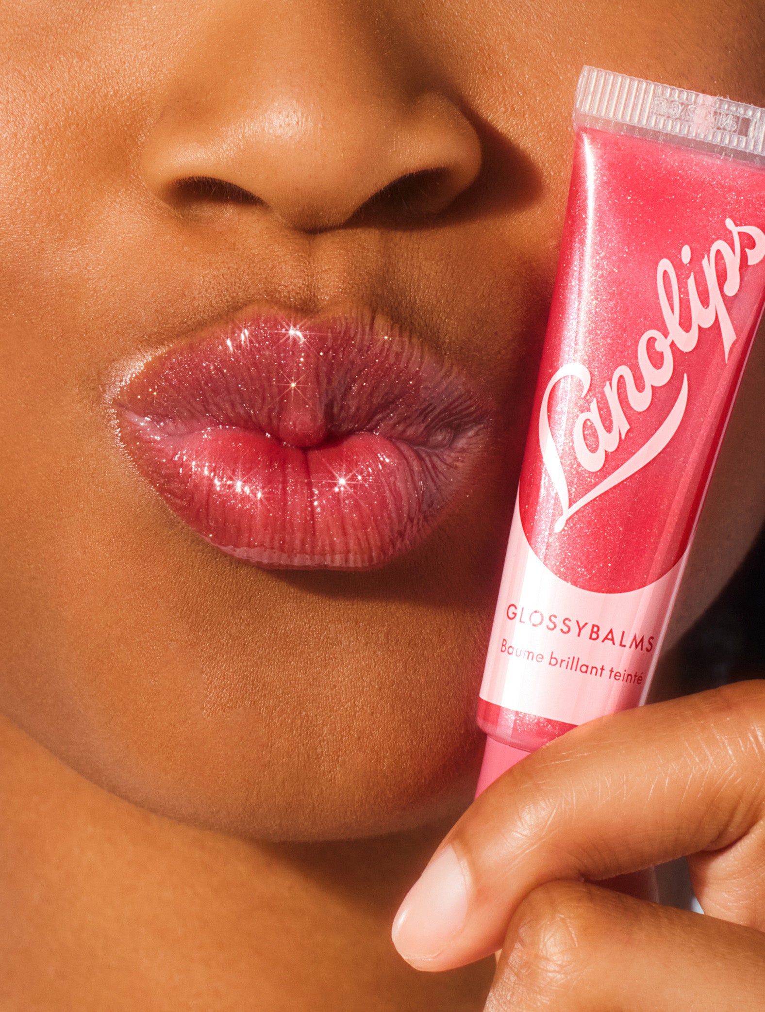 Close up image of a model holding a tube of lanolips glossy balms candy lip balm.