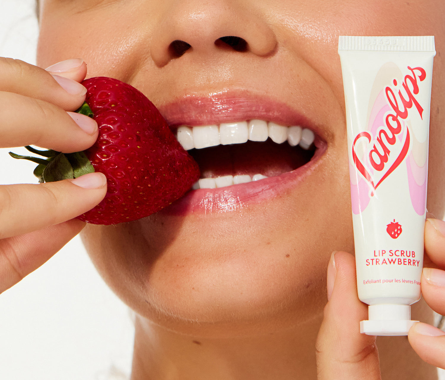 Model holding a lanolips lip scrub strawberry in her hand and a strawberry in the other.