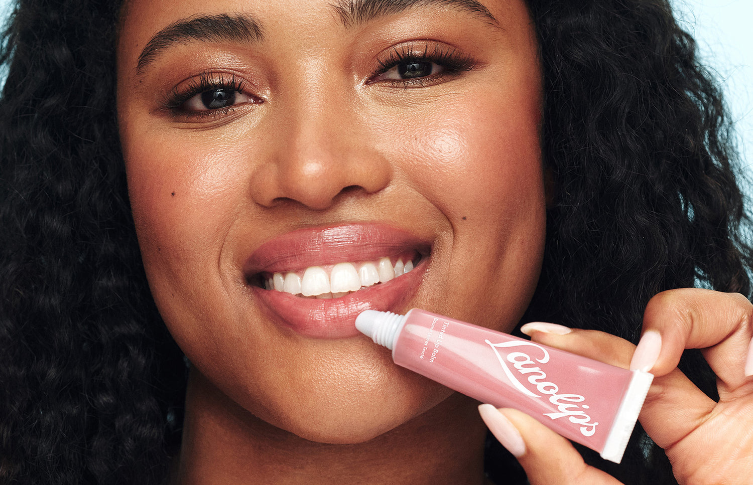 Model holding a lanolips tinted lip balm tube in her hand.