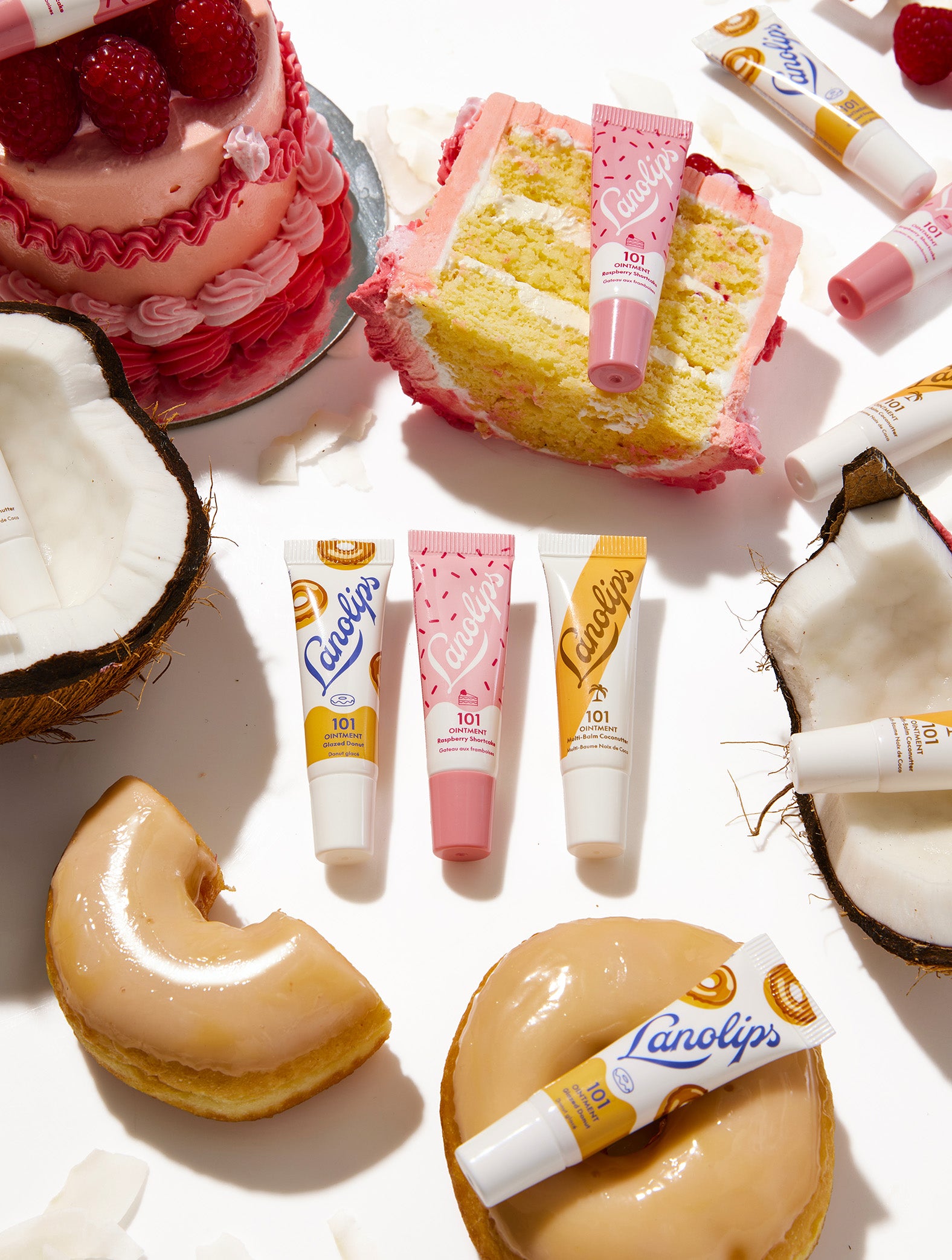 Cakes, donuts, and the Lanolips 101 Ointment mini lip balms in Glazed Donut, Raspberry Shortcake and Coconutter on a white background.