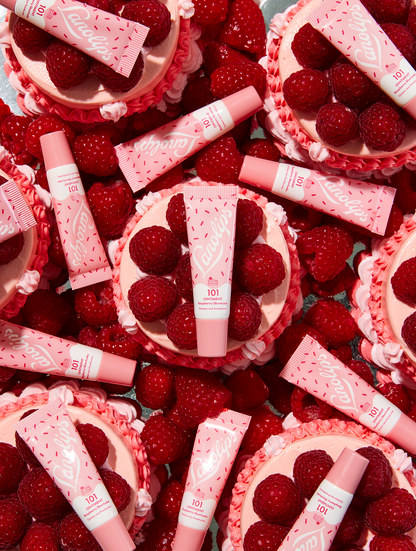 Lifestyle shot of multiple Lanolips 101 Ointment Multi-Balm Raspberry Shortcake laid on top of a raspberry shortcake cupcake. Each delicious flavor is infused with lanolin, vitamin E, and all-natural extracts that will penetrate &amp; seal in moisture to nourish and repair dry &amp; chapped lips, skin patches, cuticles elbows &amp; more.