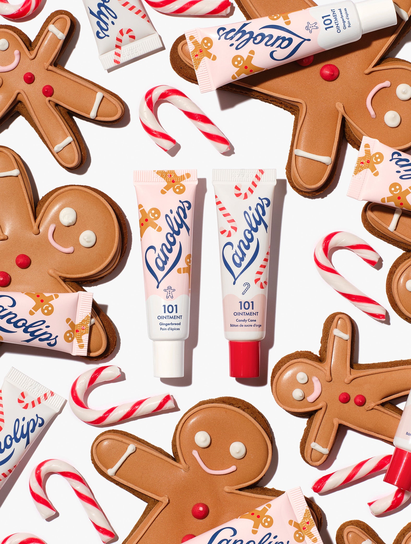 Lanolips 101 Ointment Multi-Balm Gingerbread & Candy Cane centred among gingerbread cookies, candy canes and balm tubes, from the Lanolips Holiday Gingerbread House Lip Duo. Hydrating lanolin, vitamin E and natural flavors keep lips soft and festive.