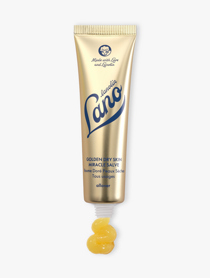 Lanolips Golden Dry Skin Miracle Salve 60g comes in a metallic gold squeezable tube with a white cap. The packaging features the Lano logo in deep blue lettering, along with ‘Made with Love and Lanolin’ inscribed at the top. A small amount of the rich, golden balm is shown oozing from the tube, emphasising its ultra-hydrating, multi-purpose formula designed to deeply nourish and repair very dry skin, hands, and rough patches.