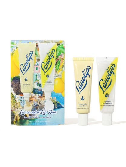 Lanolips Limoncello Lip Duo set features a tube of banana balm lip sheen and a tube of lemonaid lip treatment against a scenic Mediterranean coastal collage background with lemons.