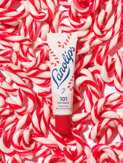 Lanolips 101 Ointment Multi-Balm Candy Cane tube on a background of red and white candy canes. Made with all-natural lanolin, vitamin-e and sweeten peppermint flavor. 