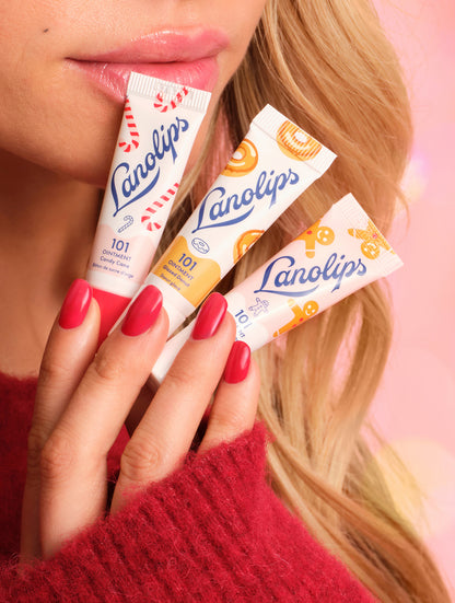 Close-up of model holding Lanolips Holiday Mini Bites lip balm trio in Candy Cane, Gingerbread and Glazed Donut flavors, with glossy lips and red nails.